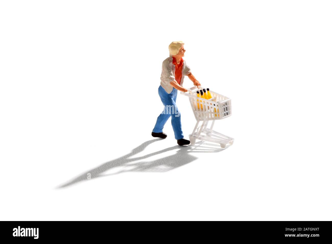 Miniaturmann schiebt einen Einkaufswagen, isoliert auf weißem Hintergrund mit Schatten Stockfoto