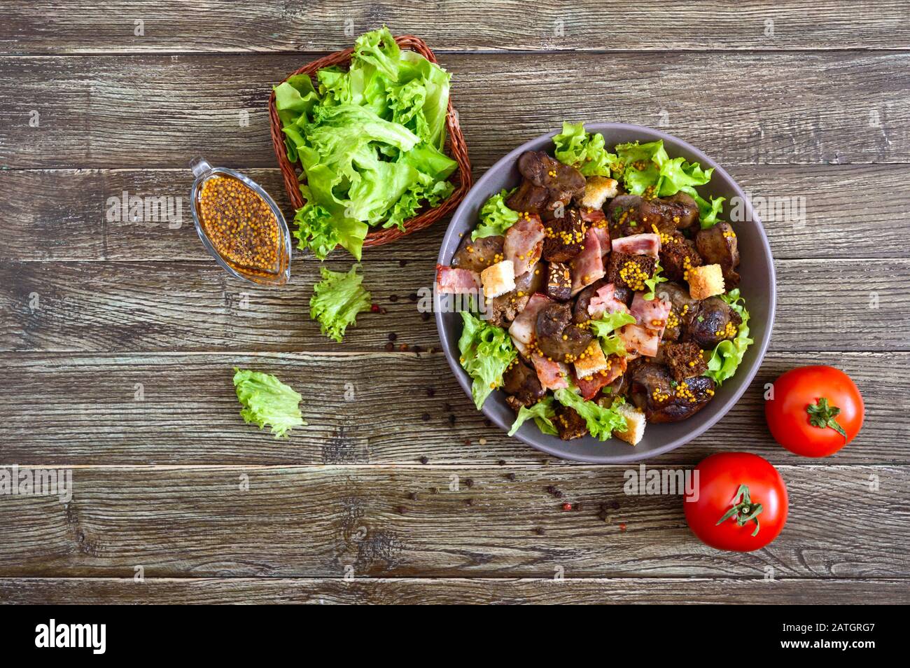 Warmer gesunder Salat aus Hühnerleber, Roggenkräuseln, geräuchertem Speck, grünem Salat und Senfsauce in einer Schüssel auf Holzgrund Stockfoto