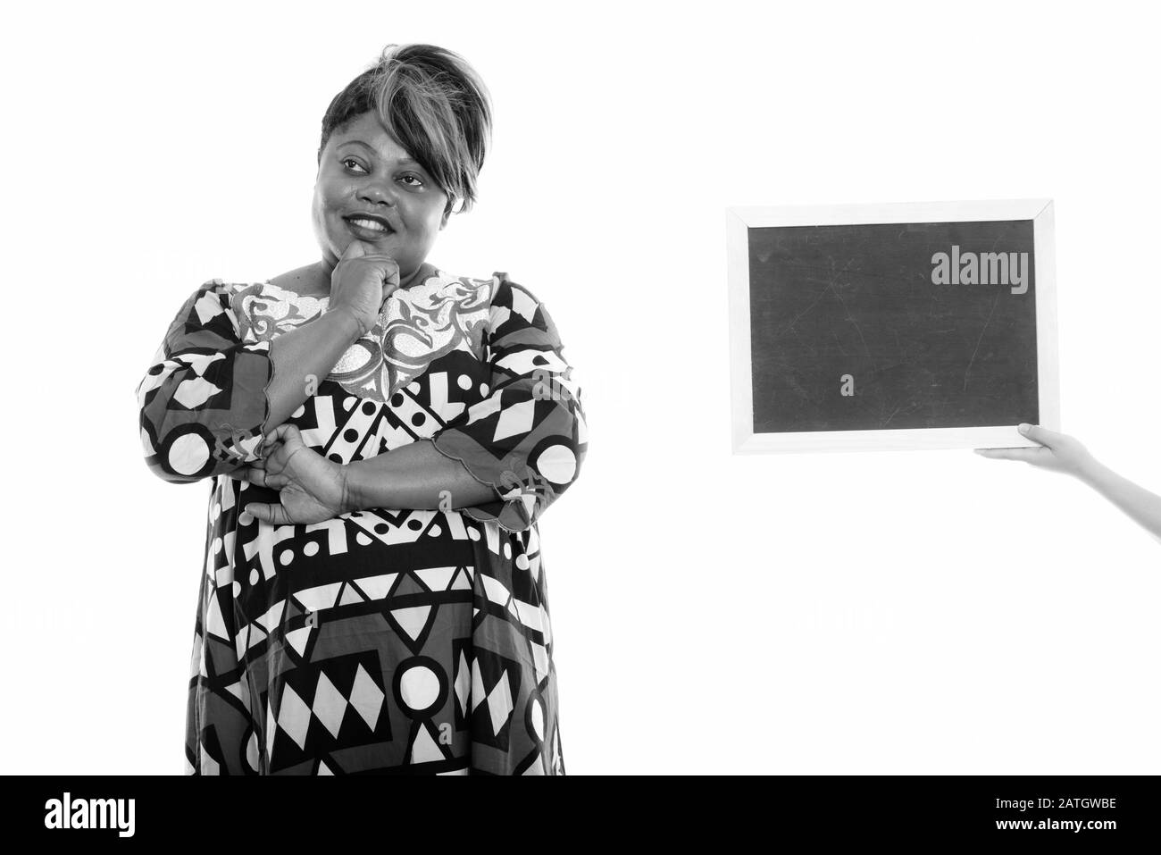 Studioaufnahme einer fröhlichen, fettreichen schwarzen Afrikanerin, die lächelt, während sie mit leerer Tafel denkt Stockfoto