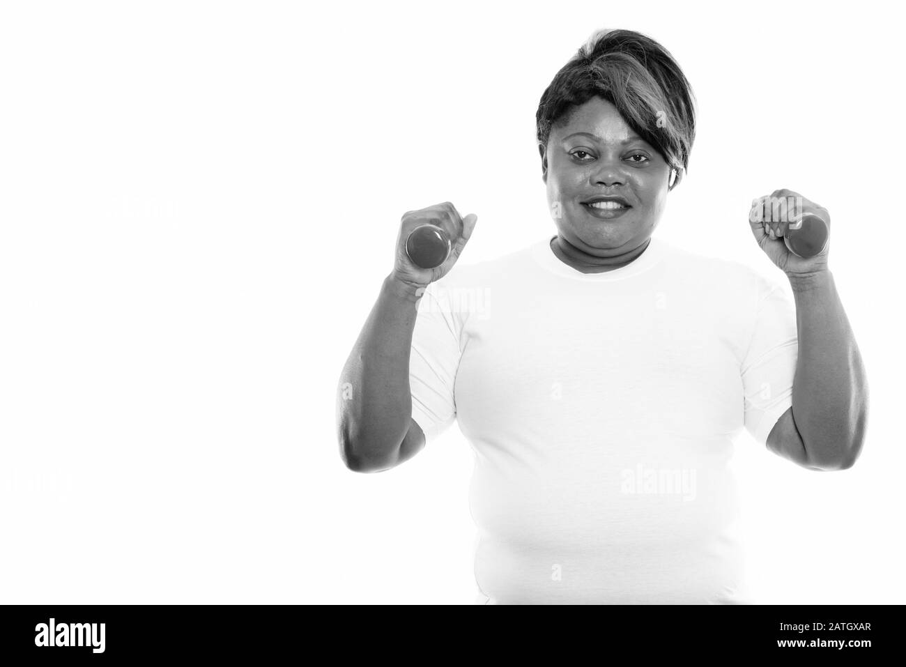 Studio-Schuss von fröhlicher, fettschwarzer Afrikanerin lächelt, während sie Hanteln für das Fitnessstudio bereithält Stockfoto