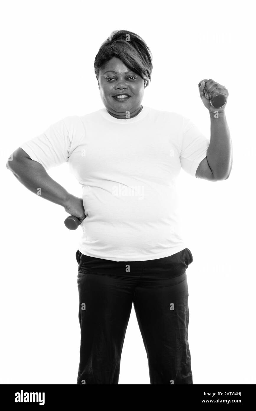 Glückliche übergewichtige Afrikanerin steht mit Hanteln in beiden Händen bereit für den Fitnessbereich Stockfoto