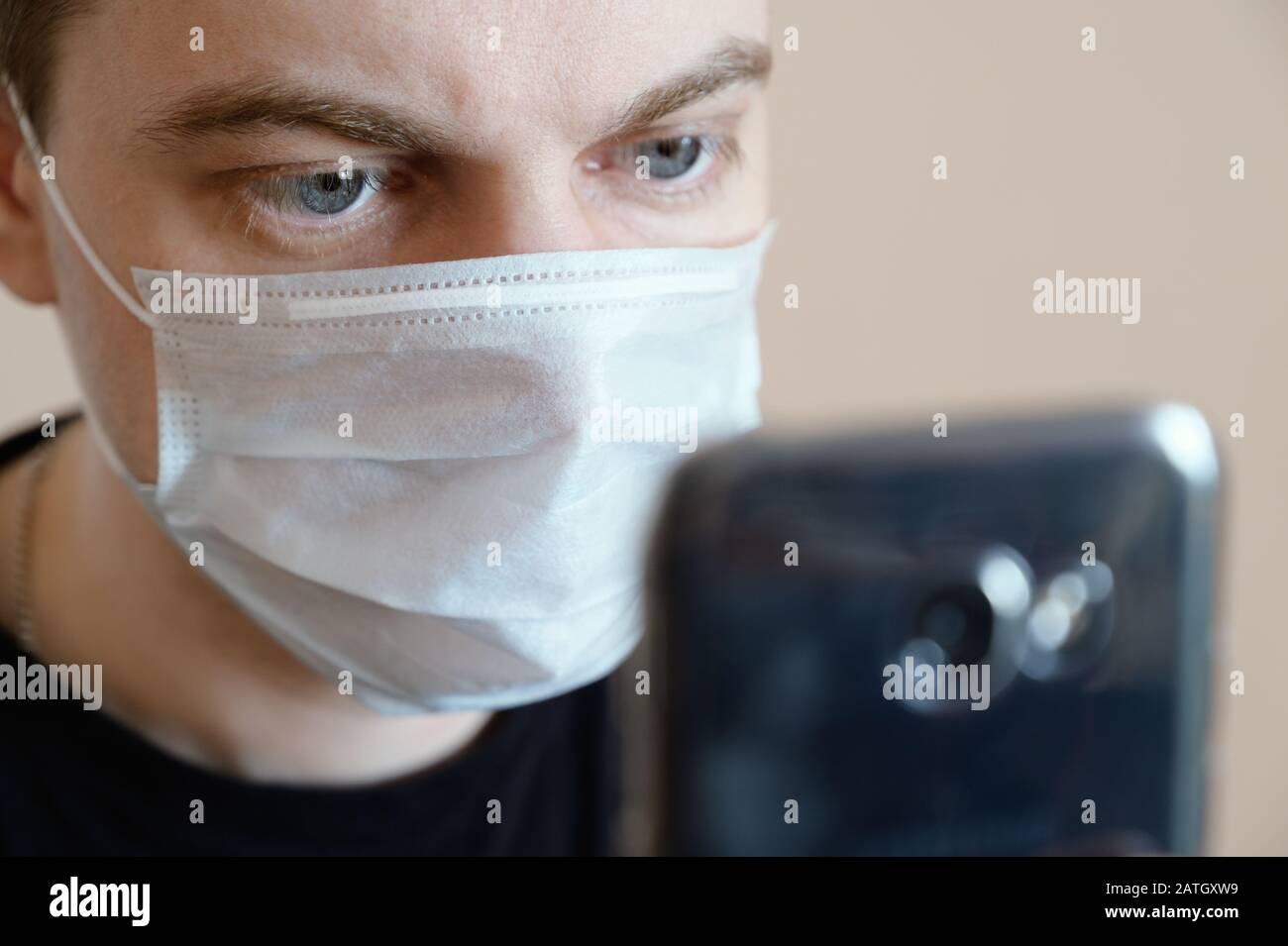 Junger Mann, der eine schützende medizinische Maske trägt und auf das Smartphone blickt. Stockfoto