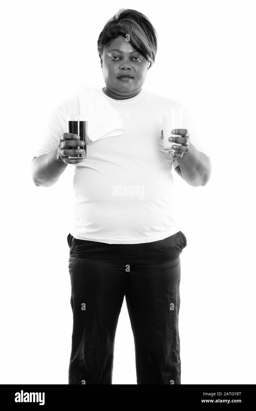Studio-Schuss von fetter schwarzer Afrikanerin steht, während sie Glas Sodagetränk und Glas Milch hält Stockfoto