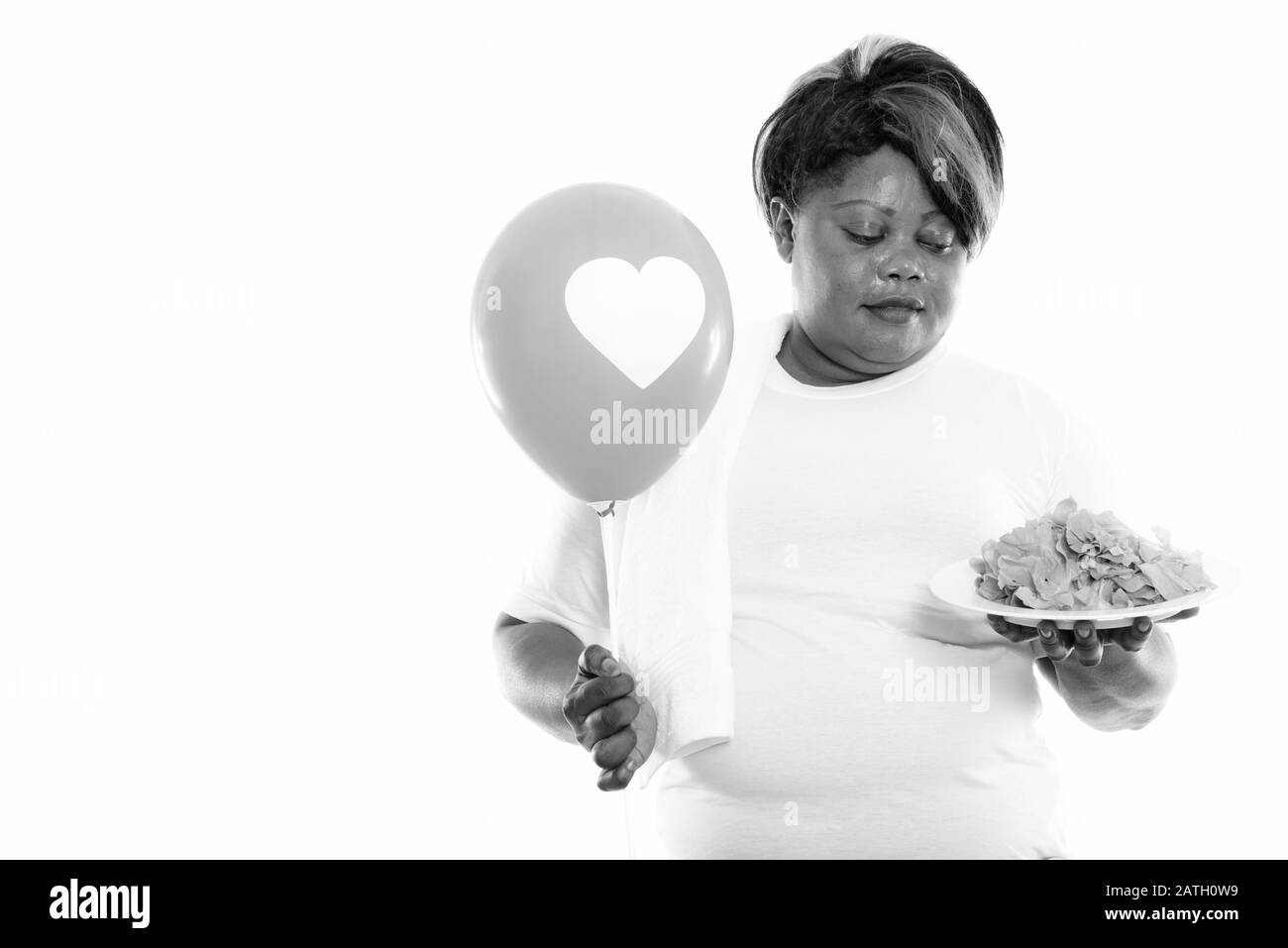 Studioaufnahme von übergewichtiger Afrikanerin, die Salat und Ballon bereit für die Sporthalle hält Stockfoto
