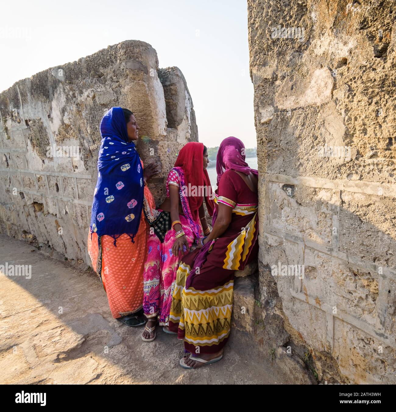 Ein ehrlicher Schuss von drei Frauen, die mit bunten, ethnischen indianischen Sarenen bekleidet sind, die auf den Wällen der alten Portugiesen sitzen, die das Diu Fort erbaut haben. Stockfoto