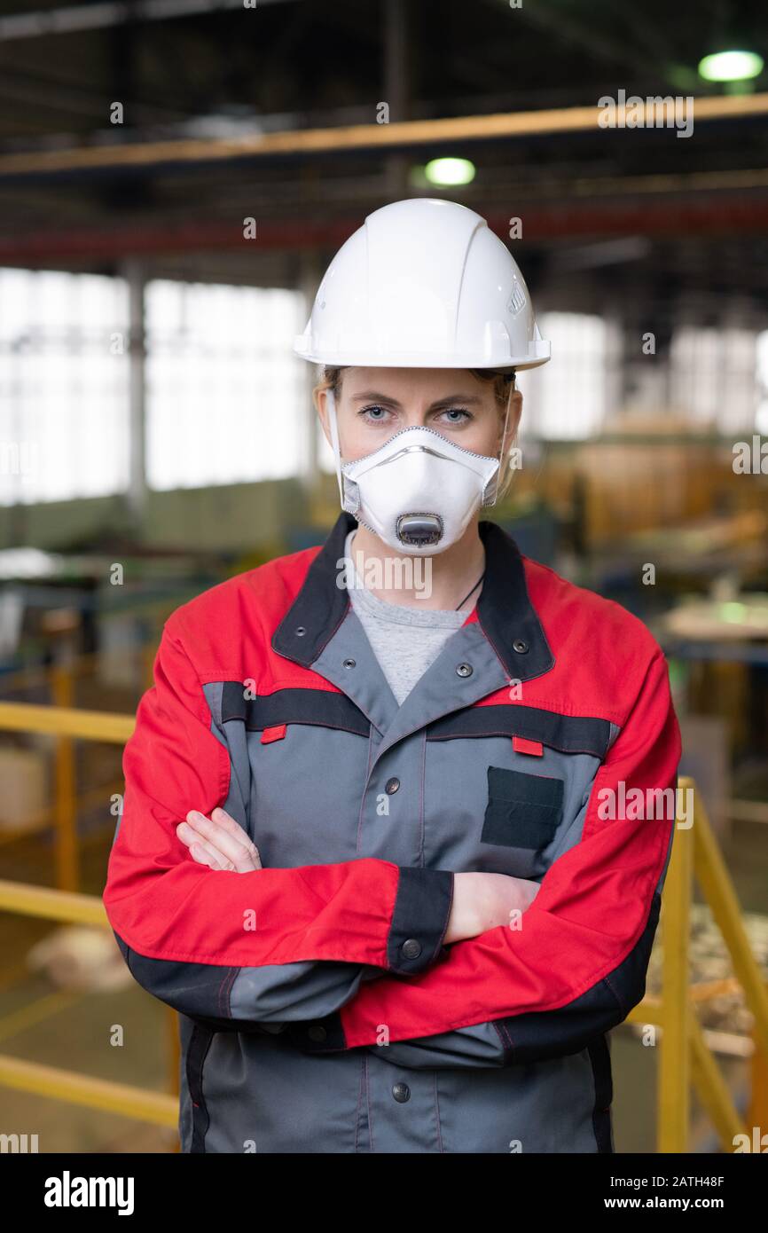 Porträt des Bauarbeiters in Atemschutzmaske und Hardhut, der mit gekreuzten Armen an der Baustelle steht Stockfoto