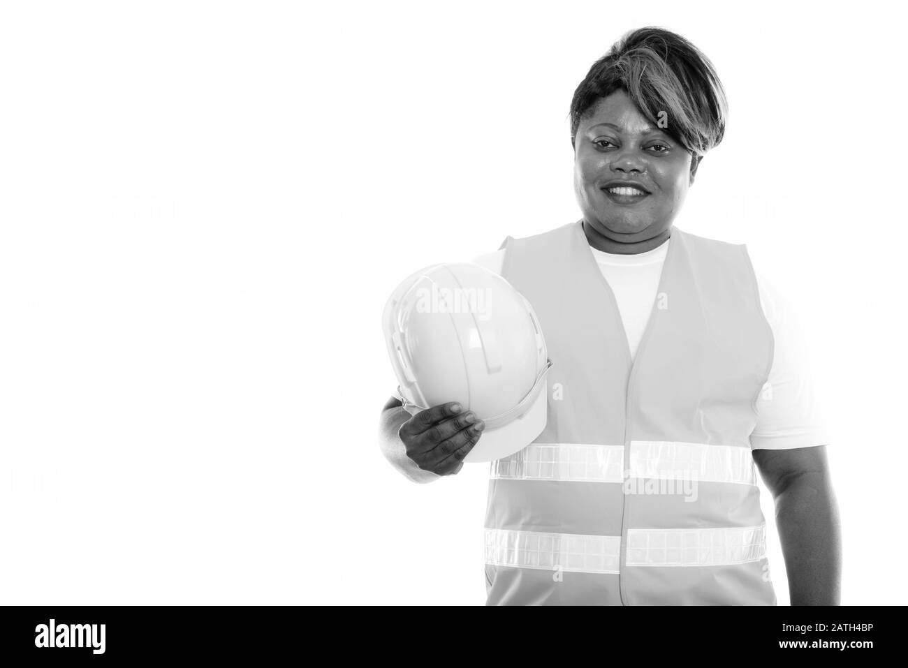 Studio Schuss von fröhlicher, fettschwarzer afrikanischer Bauarbeiterin lächelt, während sie harten Hut hält Stockfoto
