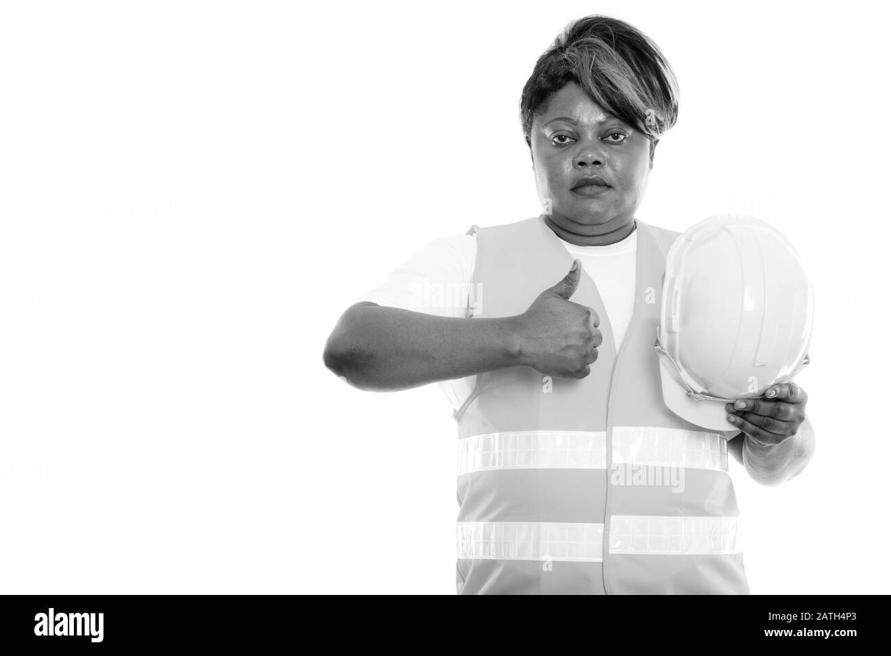 Studio Schuss von fetten schwarzen Afrikanerin Bauarbeiter hält Sicherheitshelm und gibt Daumen nach oben Stockfoto