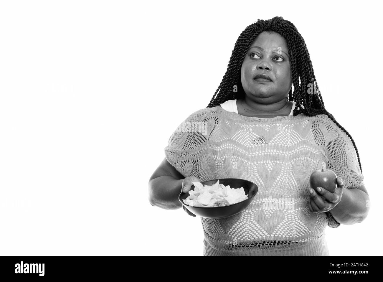 Nachdenkliche schwarze Afrikanerin mit einer Schüssel mit Kartoffelchips und apfel Stockfoto