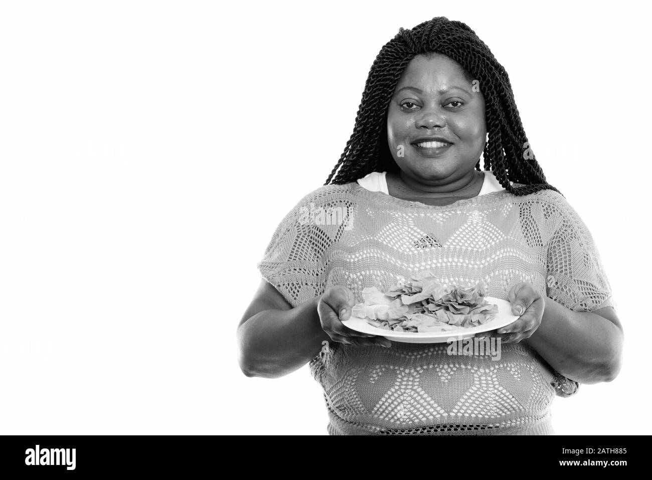 Studio-Schuss von fröhlicher, fettschwarzer Afrikanerin lächelt, während sie Salat auf weißem Teller hält Stockfoto