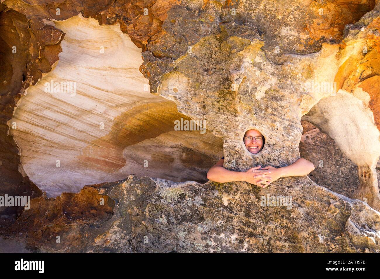 Junge lächelnde Frau, die aus einem natürlichen Loch einer bizarren Felsskulptur im Stadsaal, Cederberg Wilderness Area, Südafrika, blickt Stockfoto