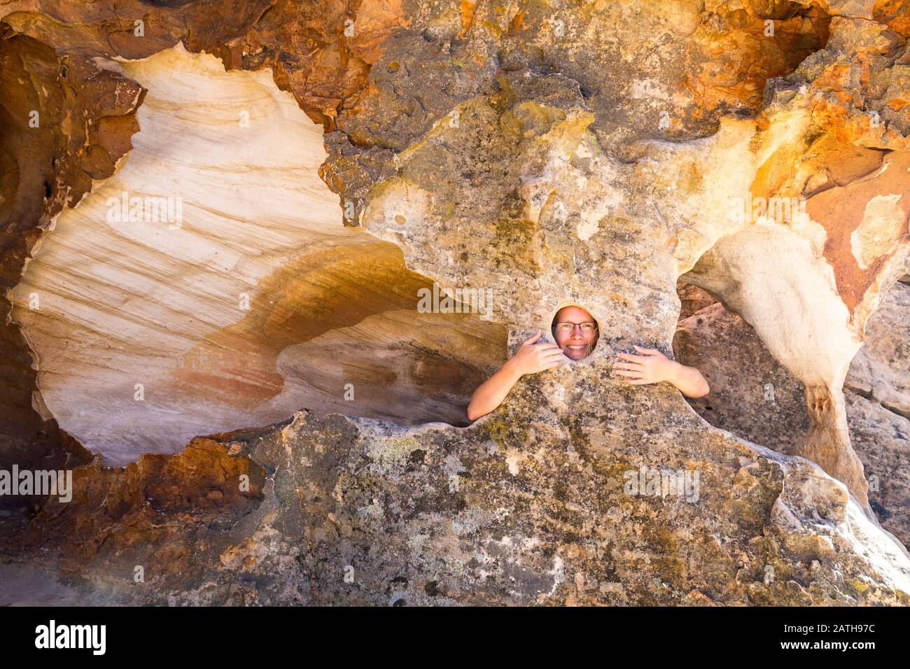 Junge lächelnde Frau, die aus einem natürlichen Loch einer bizarren Felsskulptur im Stadsaal, Cederberg Wilderness Area, Südafrika, blickt Stockfoto