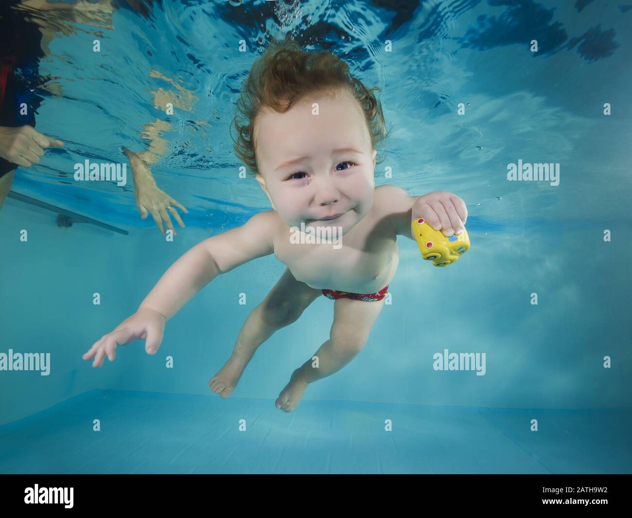 Lustiger rothaariger Junge spielt mit Spielzeug unter Wasser in einem Schwimmbad Stockfoto