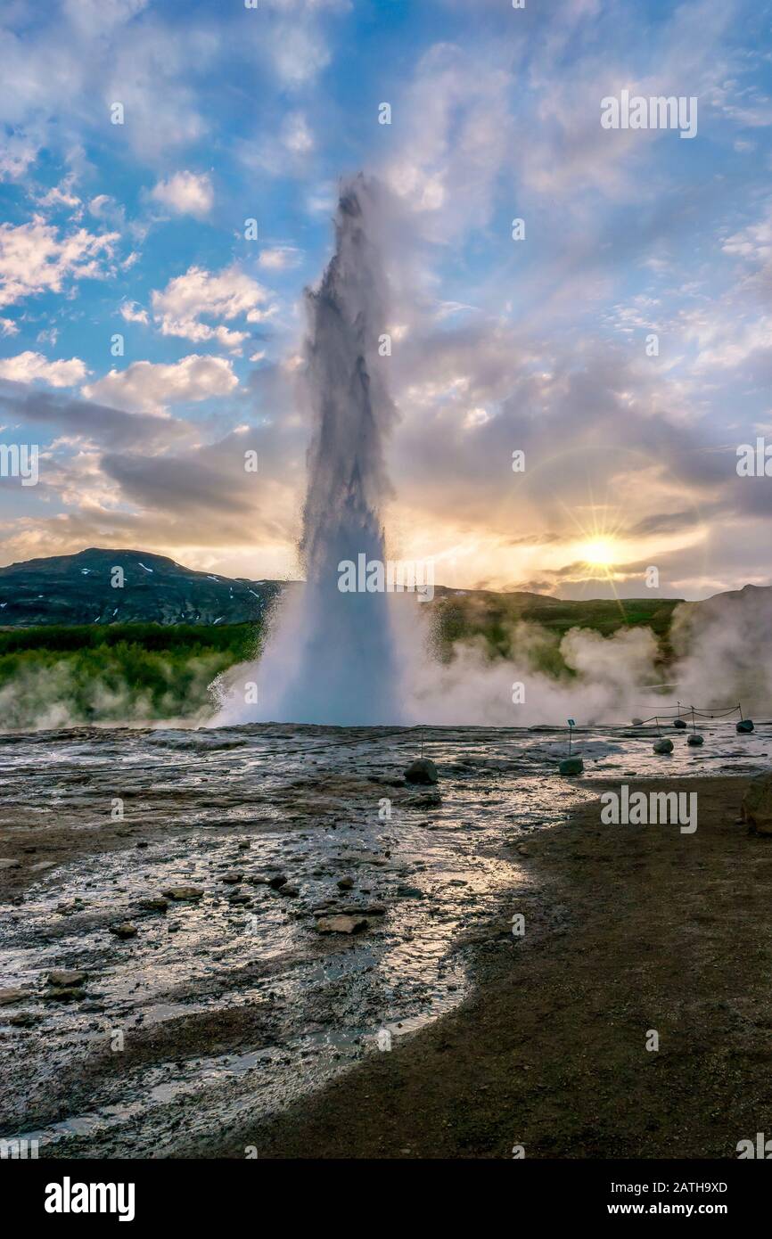 Ein vertikaler Schuss von Strokkur Geysir, einer berühmten heißen Quelle im Südwesten Islands, bricht während eines Sonnenuntergangs im Frühsommer aus. Stockfoto