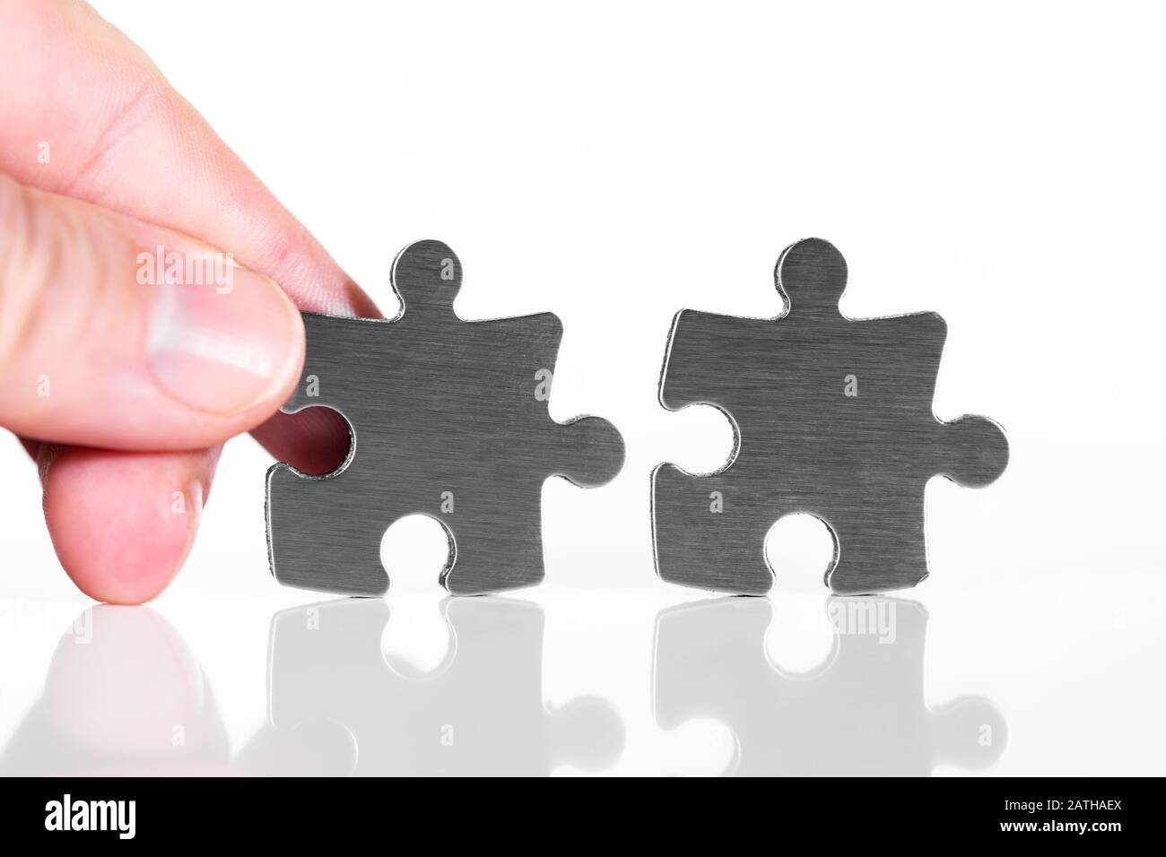 Es werden zwei Puzzleteile zusammengestellt, Nahaufnahme mit männlicher Hand, isoliert vor weißem Hintergrund Stockfoto