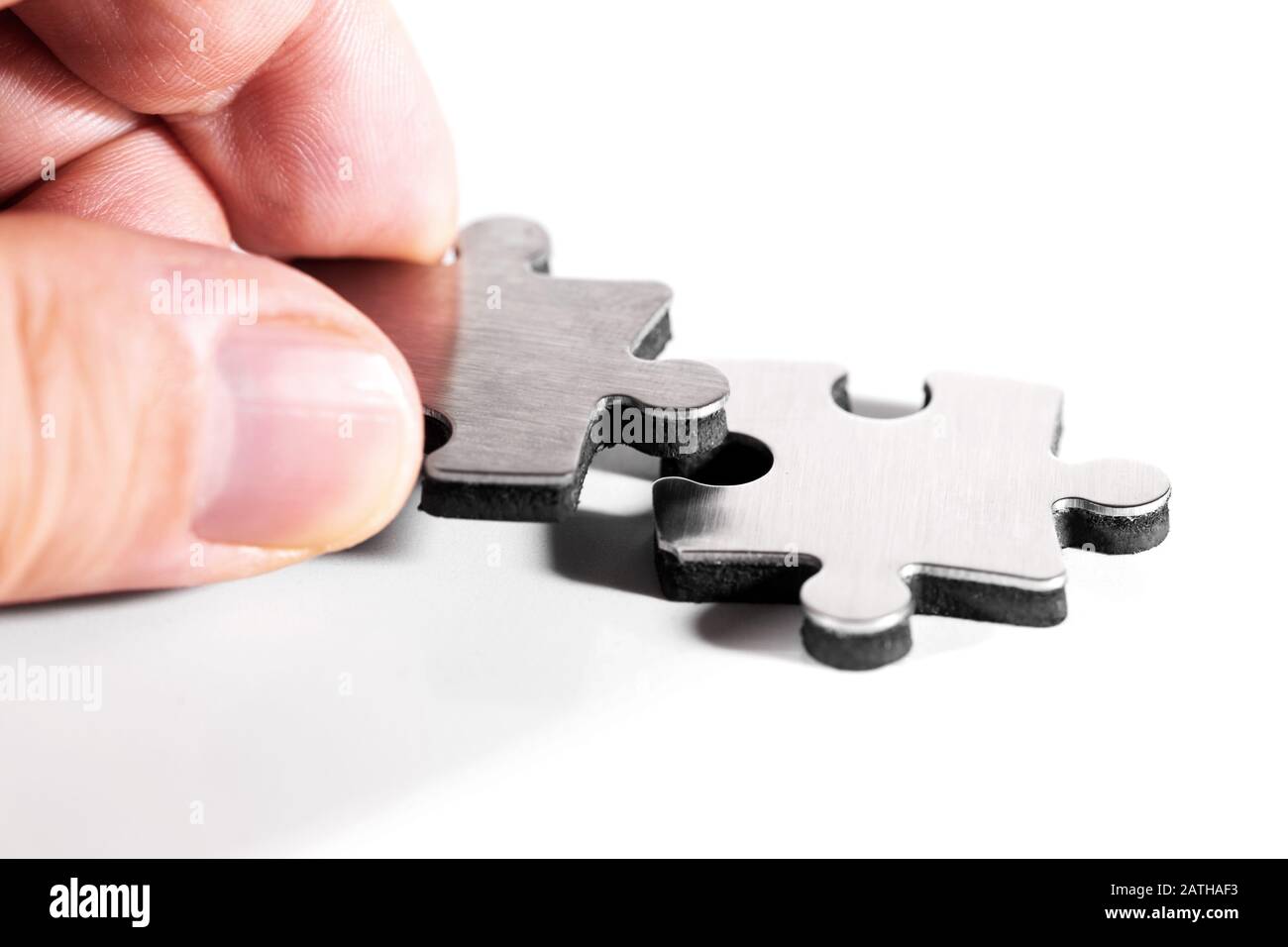 Es werden zwei Puzzleteile zusammengestellt, Nahaufnahme mit männlicher Hand, isoliert vor weißem Hintergrund Stockfoto