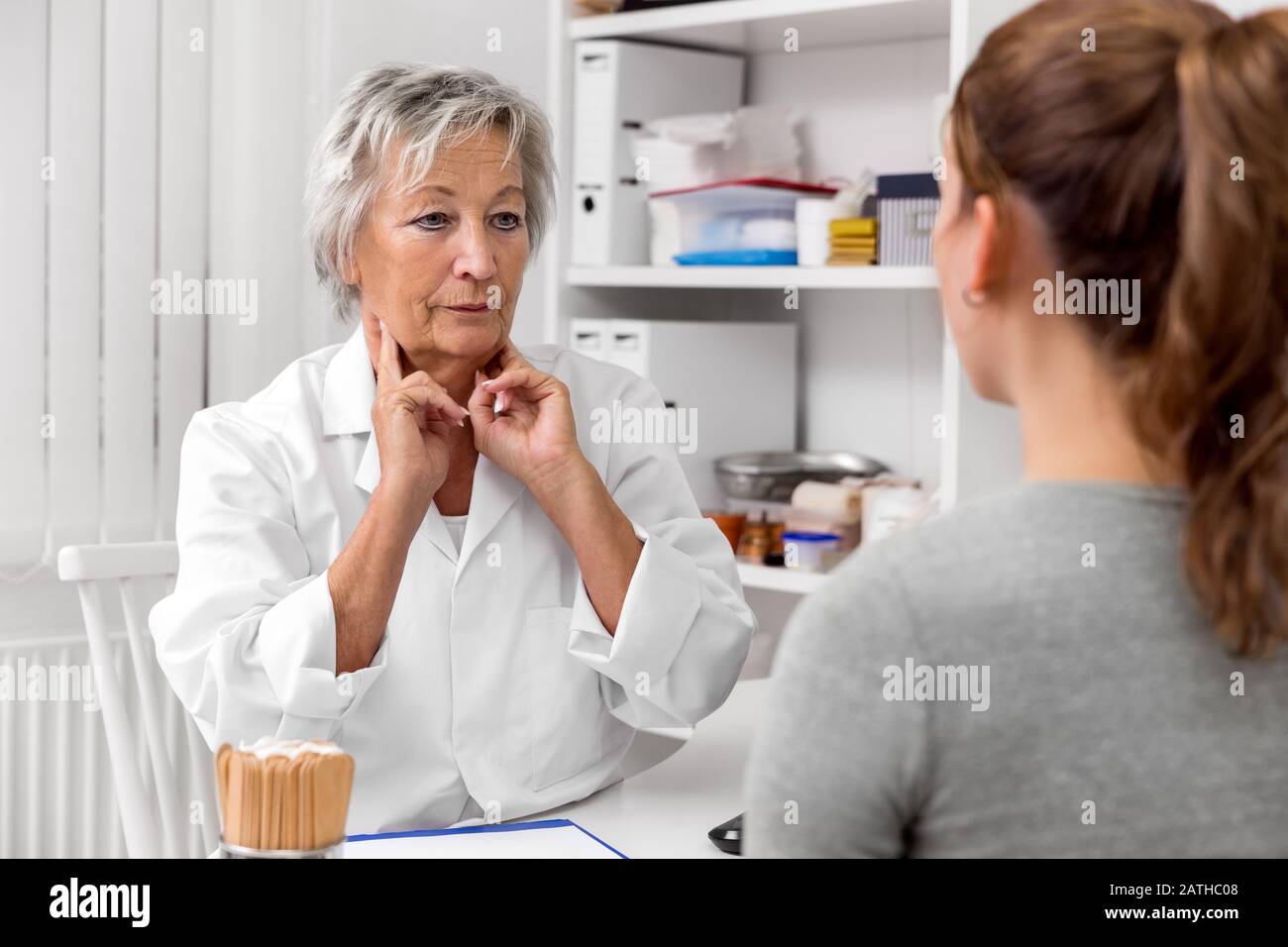 Weibliche Ärztin hält ihren Lymphknoten am Hals, Ausstellung und Demonstration für eine Patientin Stockfoto