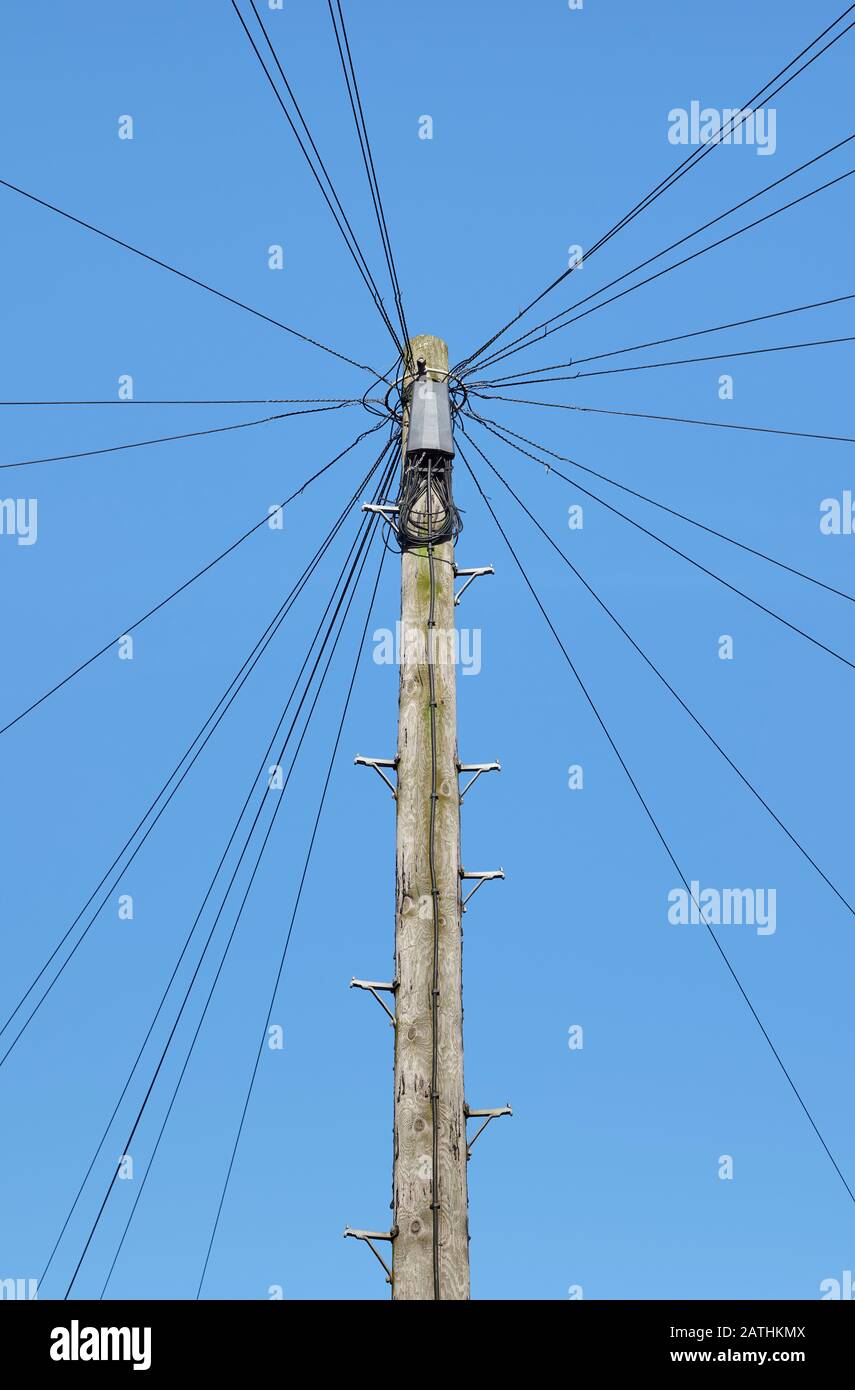 Telefonkabel, die von Holzpfosten in der städtischen Straße mit blauem Himmel abstrahlen Stockfoto