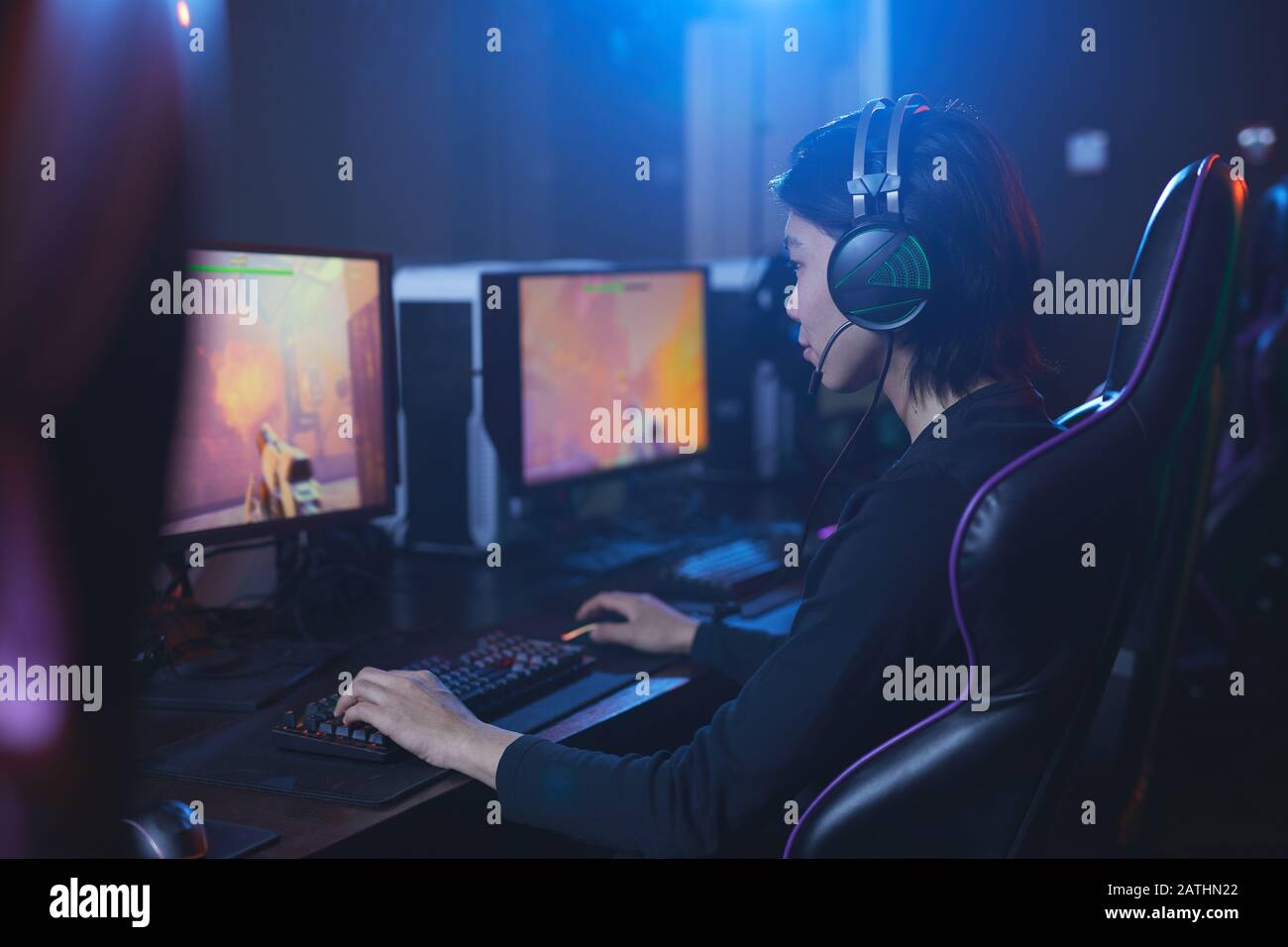 Seitenansicht Porträt des jungen Asiaten Spielen von Videospielen und tragen von Kopfhörern im dunklen Cyber-Innenraum, Kopierraum Stockfoto