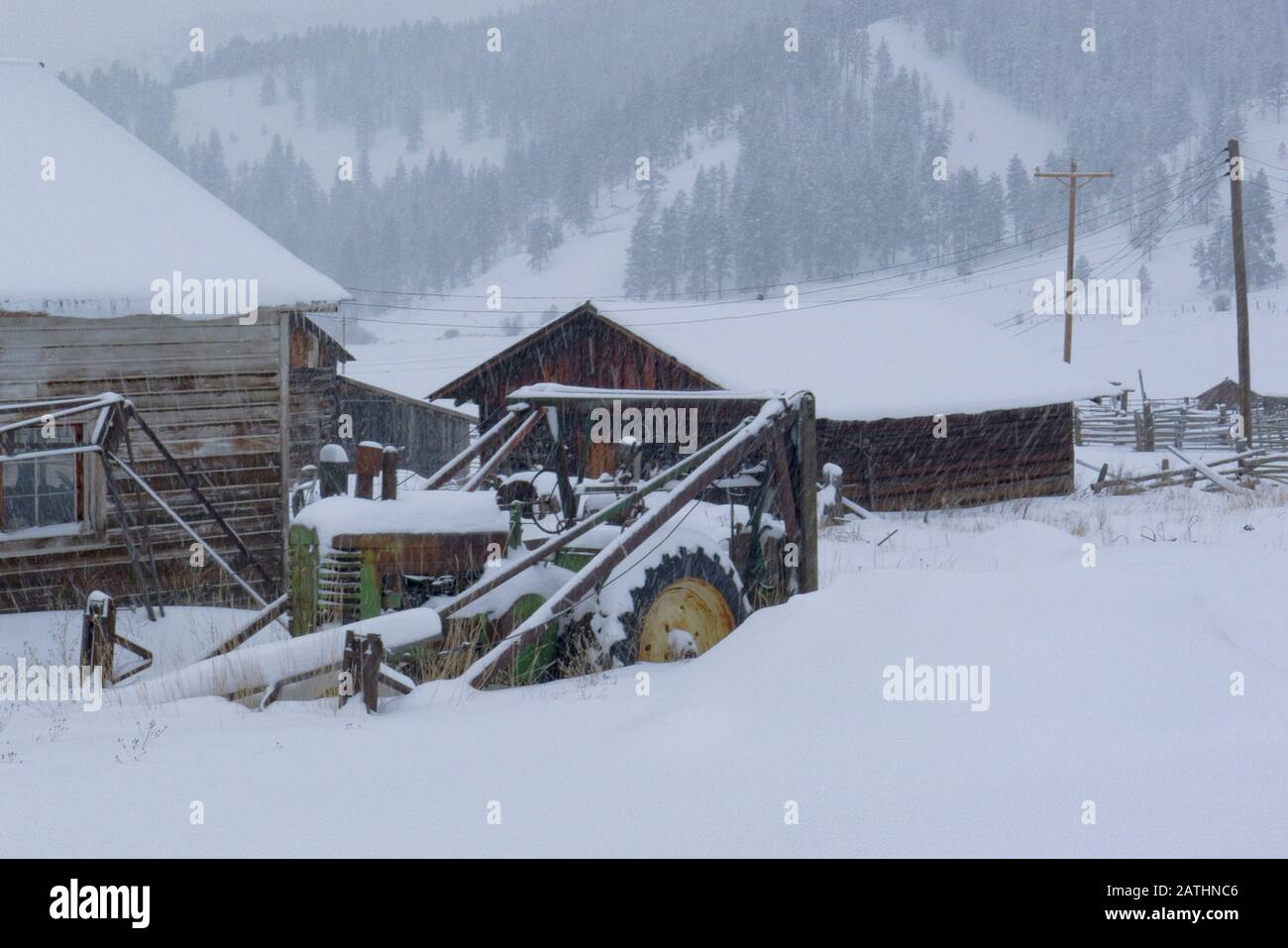 Ein John Deere Heulader-Traktor in einem Schneesturm, an der Seite einer Scheune, in Beavertail, Montana Stockfoto