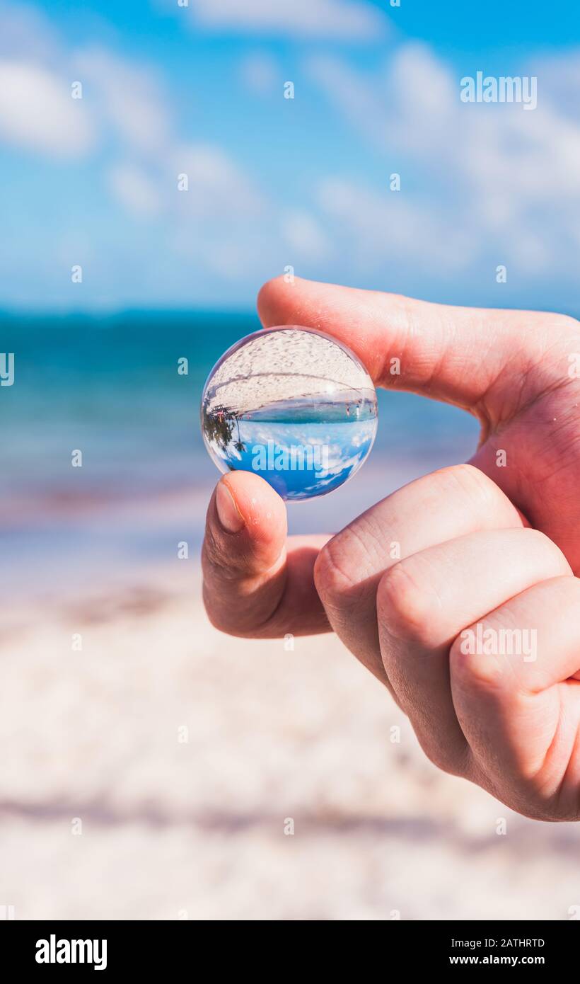 Hand hält Mini Glass Ball und Strand Hintergrund Stockfoto