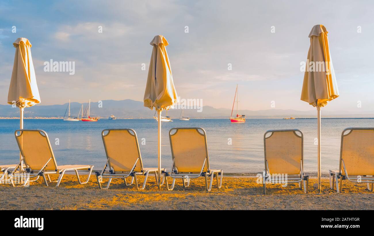 Leere Liegestühle und geschlossene Sonnenschirme an einem sandigen Strand. Reisehintergrund. Start der Saison am Strand. Schöne Landschaft und saisonale Landschaft. Postkarte, Grußkarte, Broschüre. Blick von hinten Stockfoto