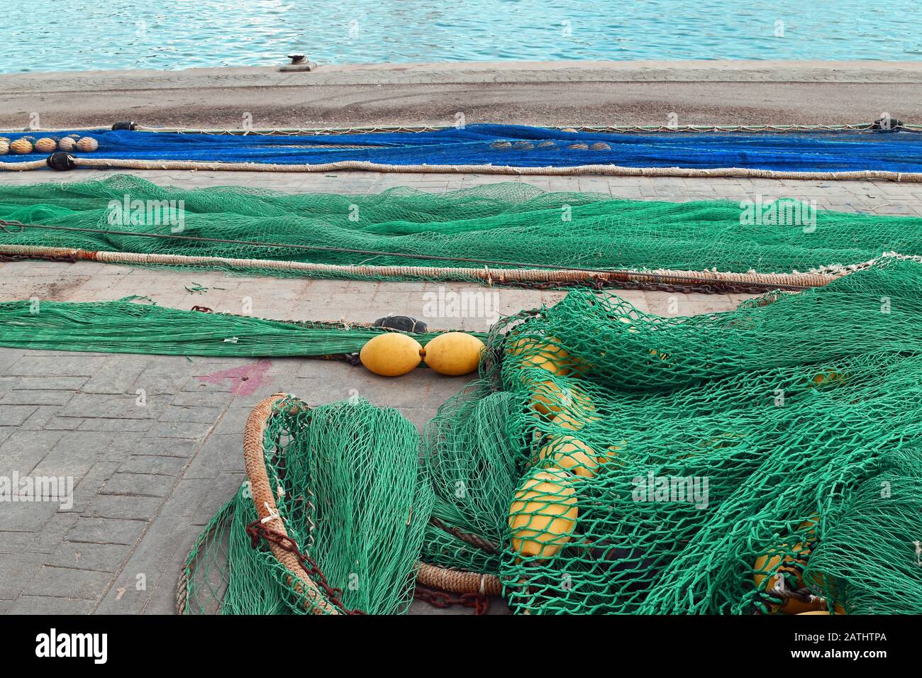 Blaue und grüne Fischernetze mit gelben Schwielen am Hafen mit Meer im Hintergrund Stockfoto