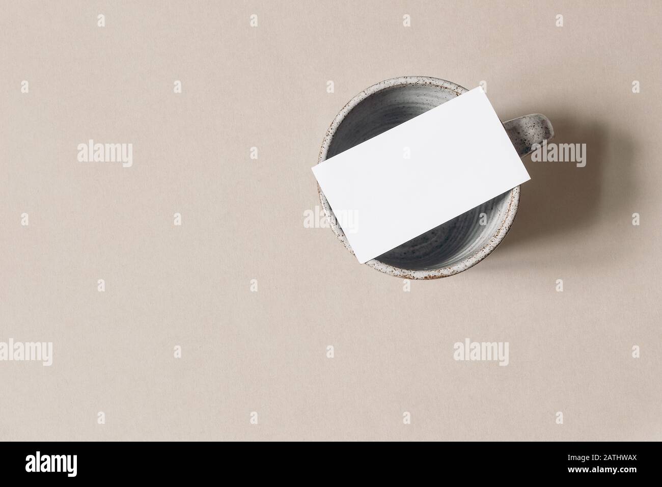 Leerer weißer Visitenkarten-Mockup auf leerer Keramikkaffeetasse. Beige Tischplatte Backgound. Modernes minimalistisches Templatemit Platz für Kopien. Markenidentität, dis Stockfoto