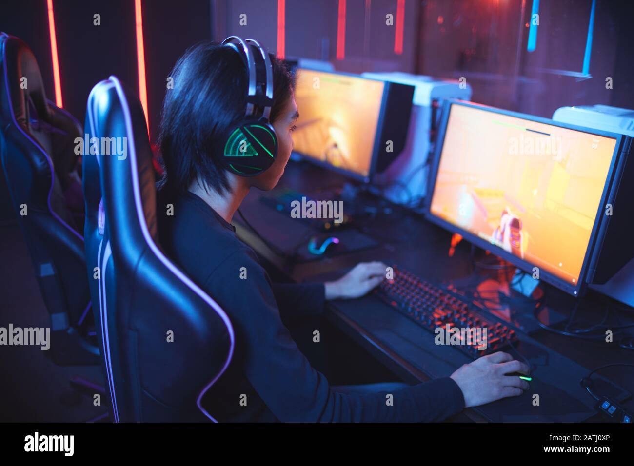 Hochwinkelporträt junger Asiaten, die Videospiele spielen und Kopfhörer im dunklen Cyber Sport-Innenraum tragen, Kopierraum Stockfoto