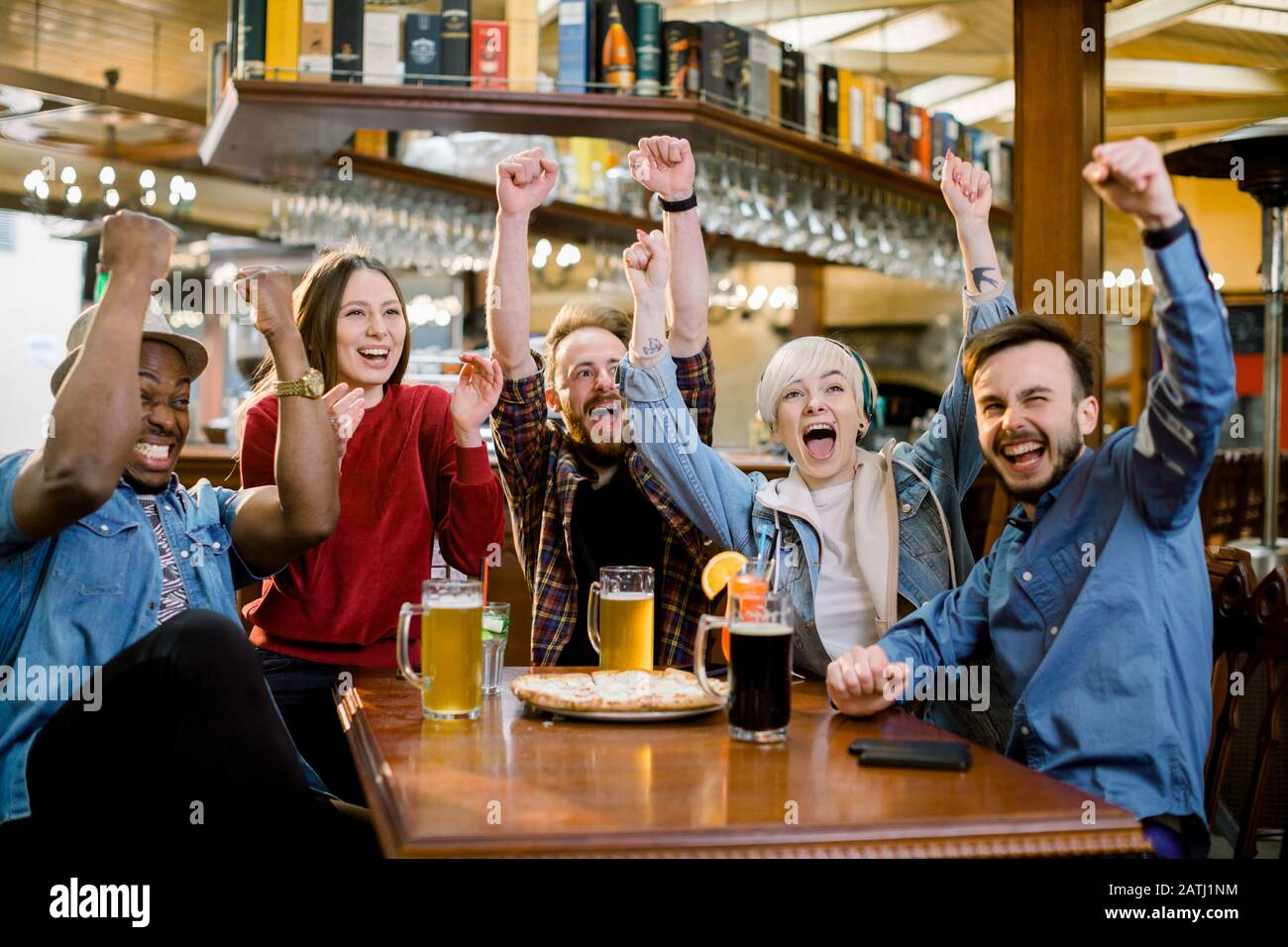 Aufgeregt diverse Freunde Fußballfans feiern Sieg Torpunktzahl Online-Spiel im fernsehen im Café, das das Siegerteam beim Bieressen unterstützt Stockfoto