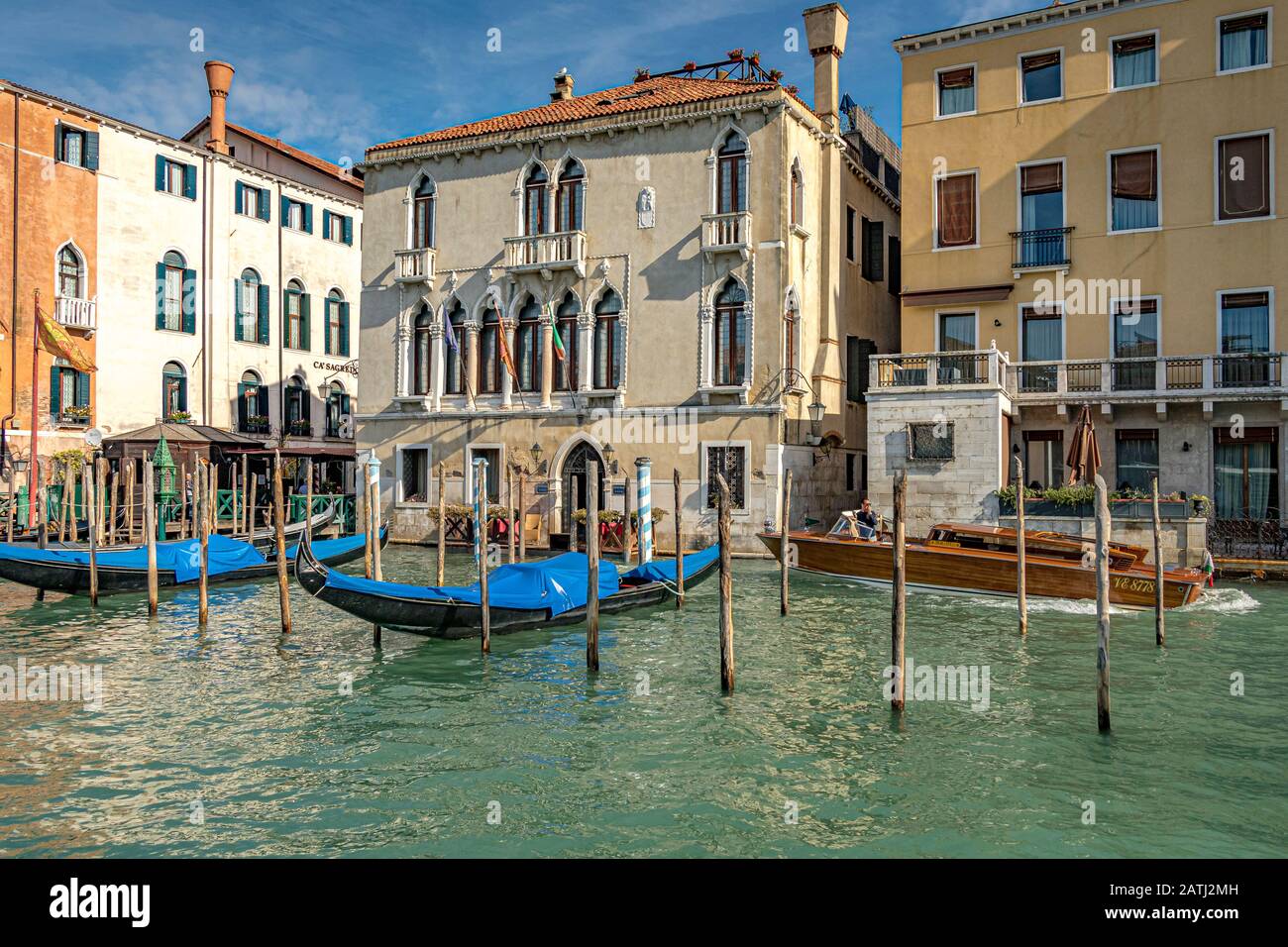 Ein Wassertaxi führt an zwei leeren Gondeln vorbei, die auf Holz-Anlegestellen am Canal Grande, Venedig, aufliegen Stockfoto