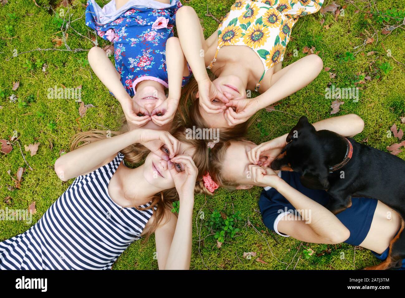 Mädchen verschiedener Altersgruppen, die in einem Sommerwald zusammen auf einem Moos liegen und die Sommerferien im Freien genießen Stockfoto