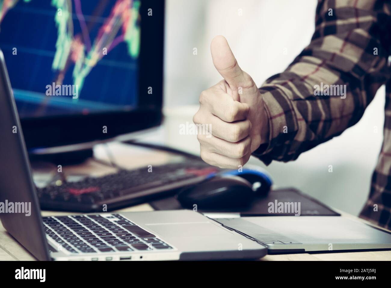 Daumen nach oben mit einem Laptop und einem Kursdiagramm im Hintergrund. Stockfoto
