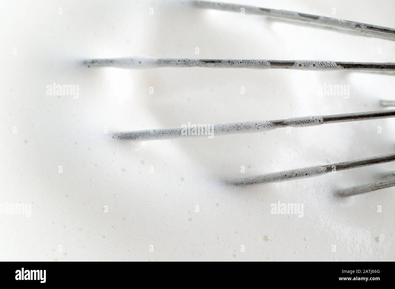 Nahaufnahme (Makro) des Metallballons, der aufschäumende Aquafaba (veganer Eiweißaustauscher) anpeitscht. Luftblasen sichtbar. Stockfoto