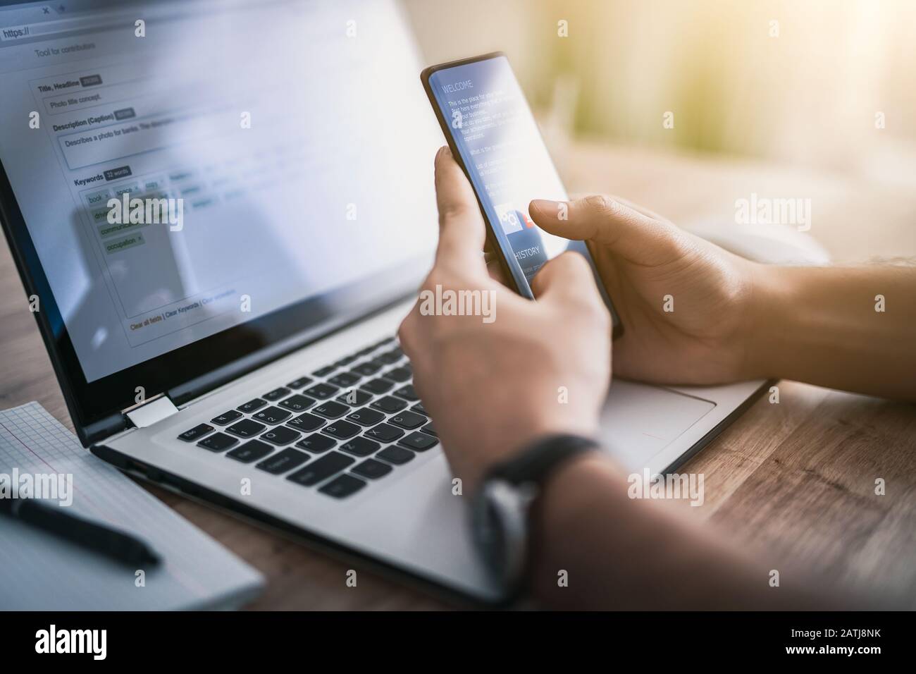 Der Mann arbeitet zu Hause und verwendet ein Smartphone und einen Notebook-Computer. Silhouette eines geschäftigen Mannes. Die eine Hand hält und verwendet das Telefon, die andere schreibt an Stockfoto