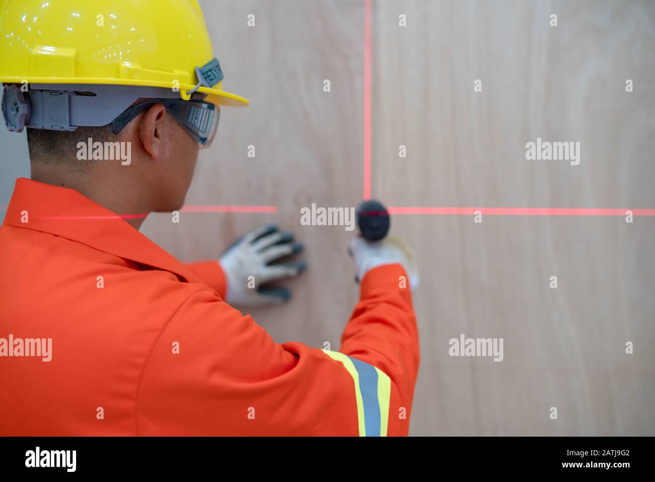Der Techniker arbeitet daran, die Wand mit einem elektrischen Bohrer entsprechend dem Markierungspunkt der Laser-Füllstandsmaschine zu bohren Stockfoto