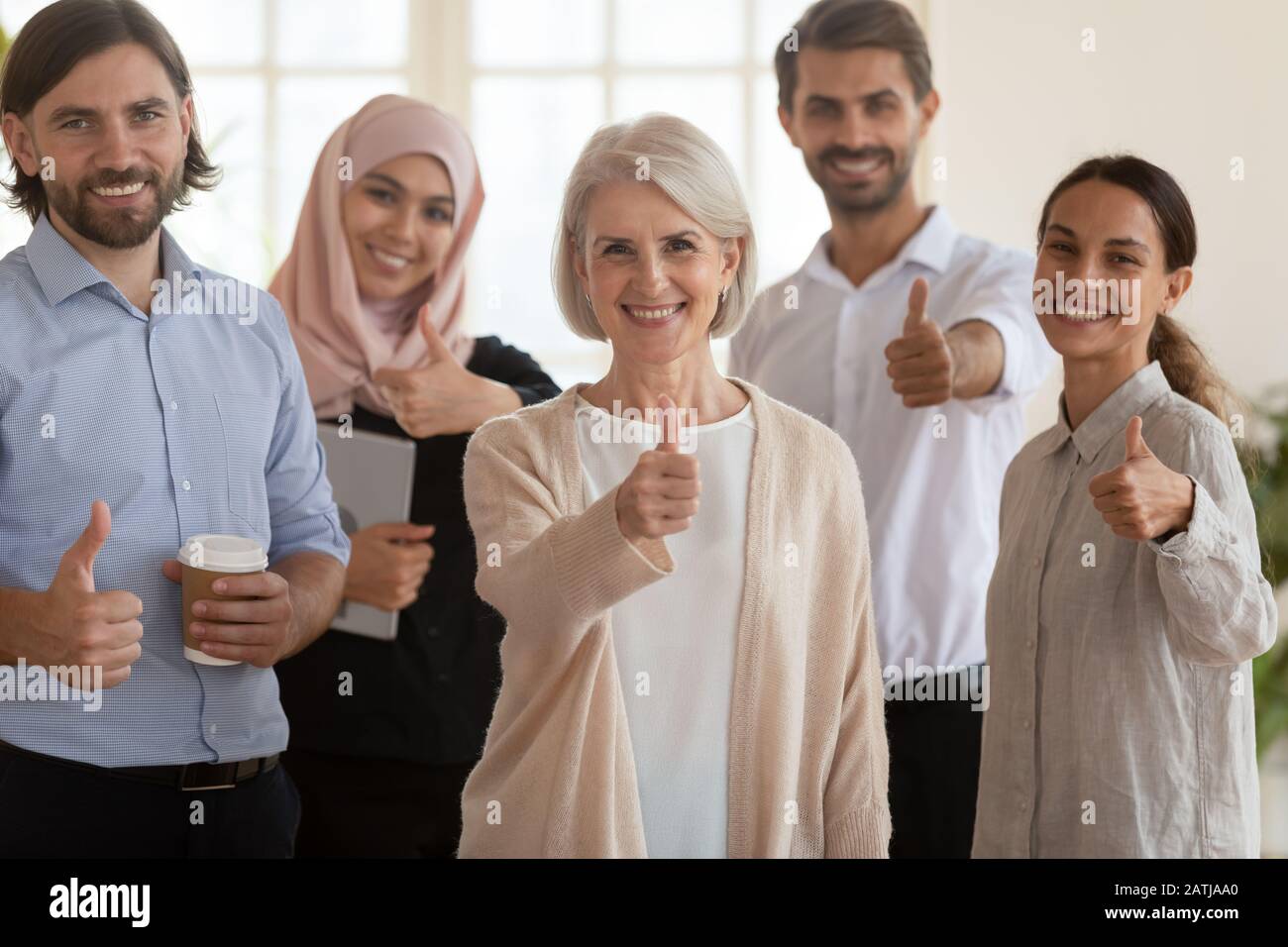 Fröhliche multiethnische Kollegen zeigen, dass sich die Daumen im Büro sammeln Stockfoto