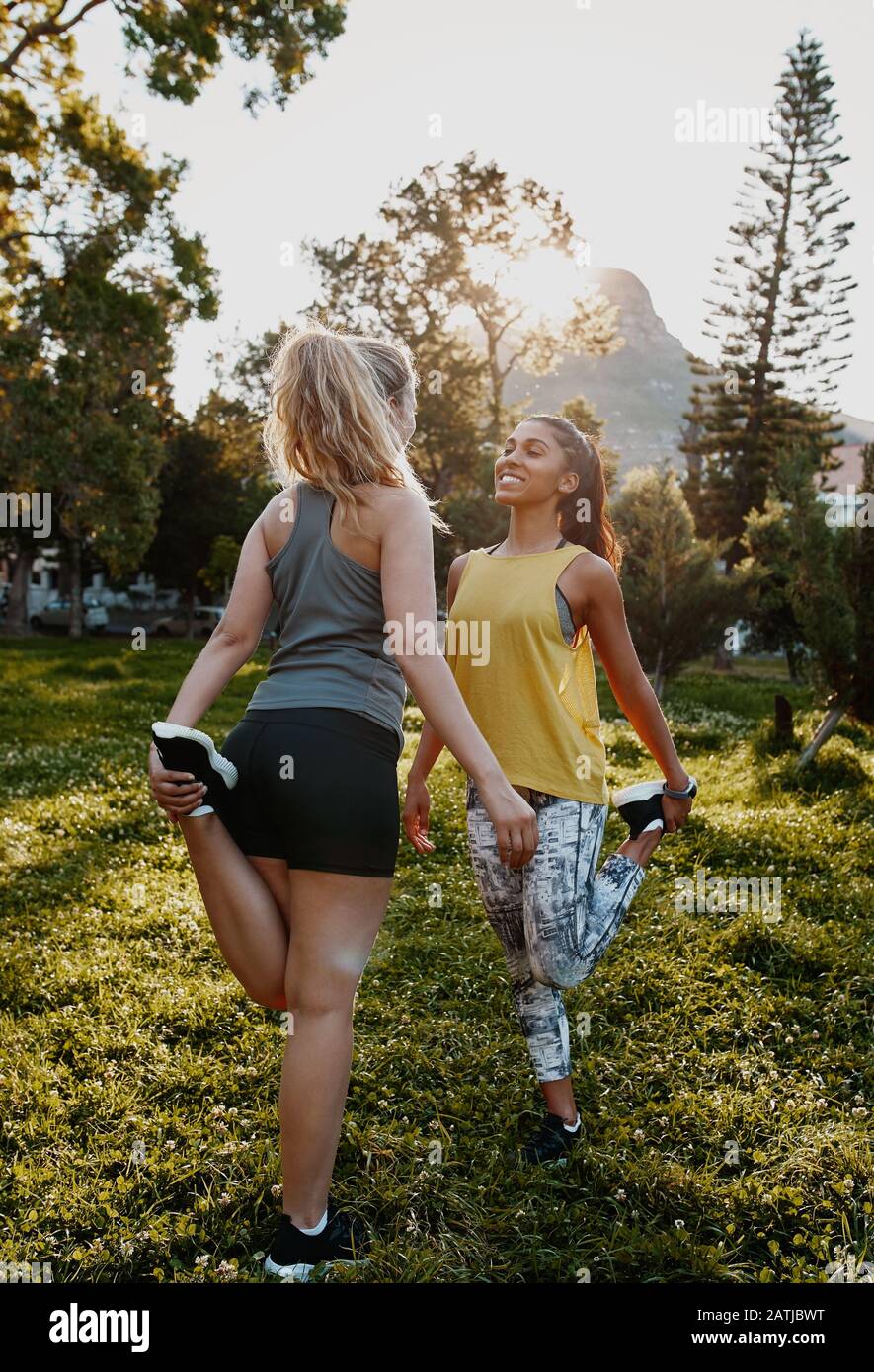 Lächelnde Sportlerin, die mit ihren Freunden im Park Dehnübungen macht - zwei Freunde, die im Park trainieren Stockfoto