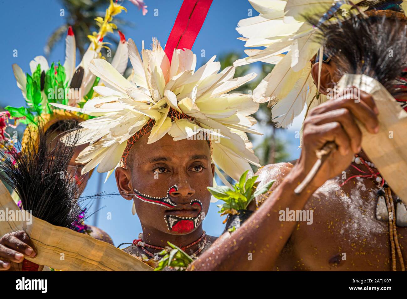Ein Tänzer, der einen weißen Federkopfschmuck mit einem roten Band am Hinterkopf trägt, blickt seitwärts mit gesenktem Blick während des traditionellen Milamala-Tanzes der Trobriand-Inseln in Kwebwaga, Papua-Neuguinea. Stockfoto