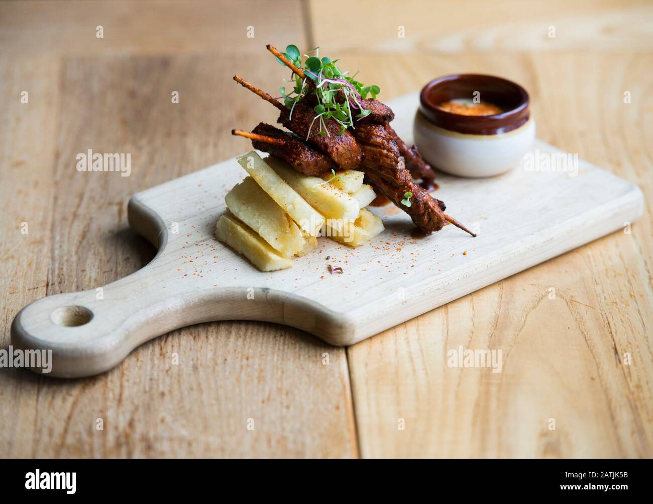 Anticucho Beef Spieße mit Yuka Pommes und tari Sauce werden auf einem Tisch in einem Restaurant gezeigt Stockfoto