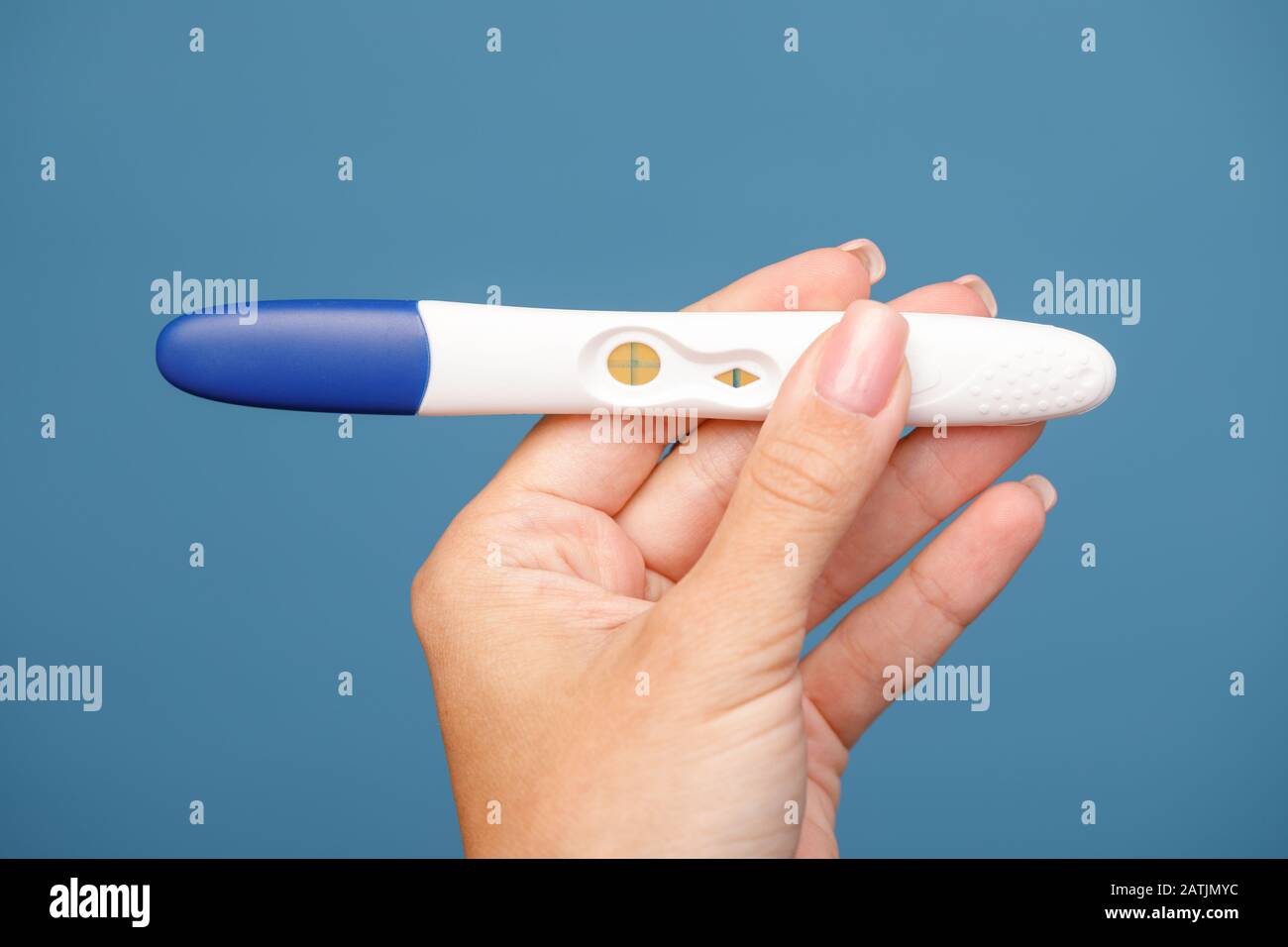 Studio shot der Hand junge Frau mit Schwangerschaftstest mit positiven Schwangeren Ergebnisse vor blauem Hintergrund Stockfoto