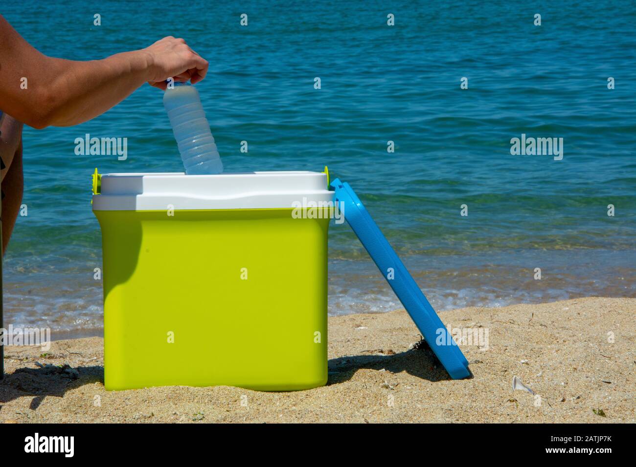 Ein menschlicher Arm nimmt eine Flasche Wasser aus dem tragbaren Kühlschrank Stockfoto