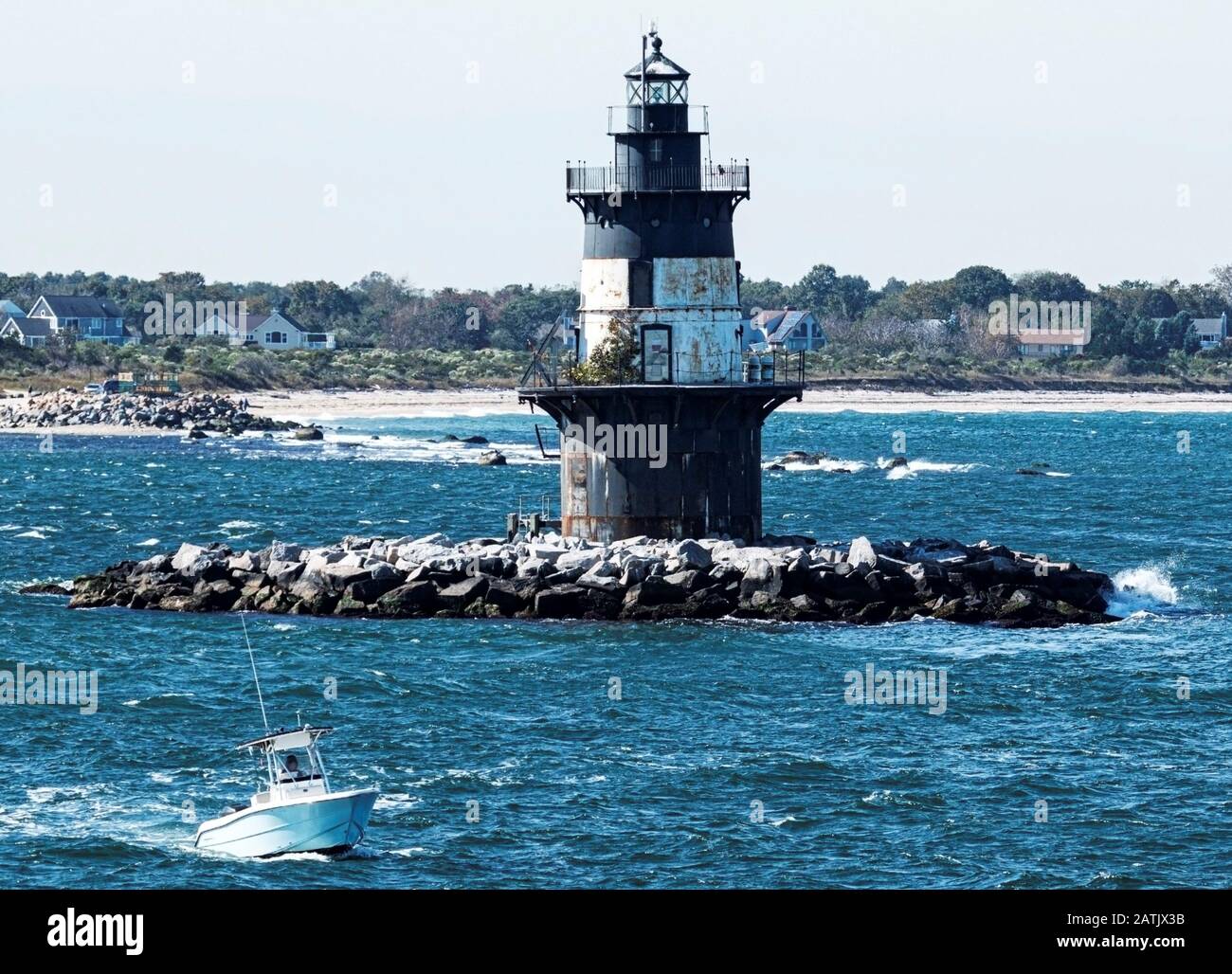 An einem windigen Tag mit rauer See und dem Strand im Hintergrund passiert ein Boot den Orient Point Lighthouse. Stockfoto