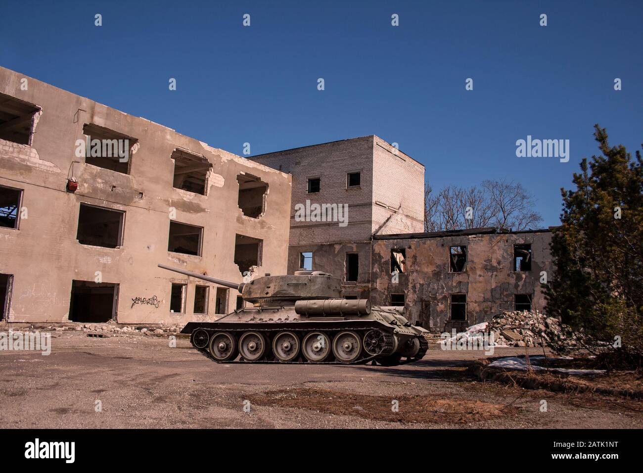 Eine Kriegsschaupzene eines einzigen Panzers, der in der Stadt von einem großen abgerissenen Haus unter einem wolkenlosen klaren blauen Frühlingskimmel durchquält wird und zum Angriff bereit ist Stockfoto