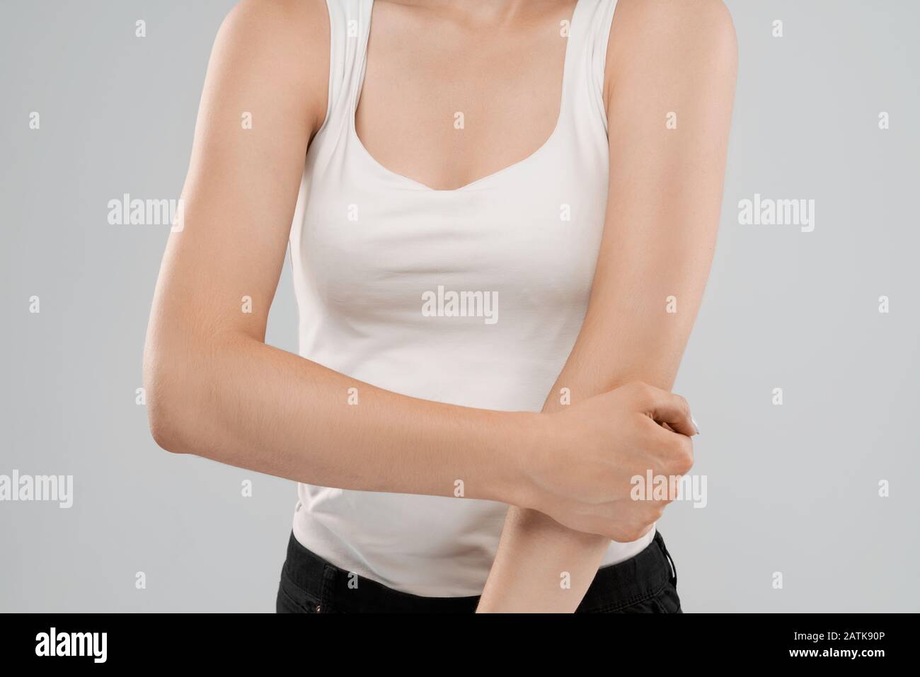Clolse von Incognito kaukasische Frau in weißem Hemd Posing über Grau isoliert Hintergrund und Ellenbogen berühren, weil der Schaden. Crop von brunette leiden unter Schmerzen im Arm. Stockfoto