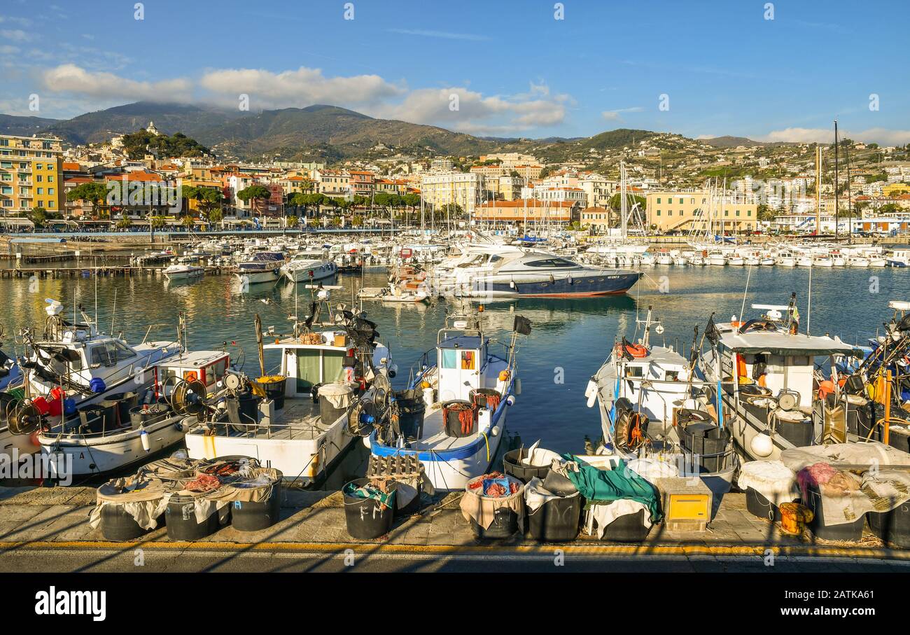 Malerische Aussicht auf den Hafen mit Fischerbooten und Luxusyachten, die an den Piers und der Küstenstadt im Hintergrund angedockt sind, Sanremo, Ligurien, Italien Stockfoto