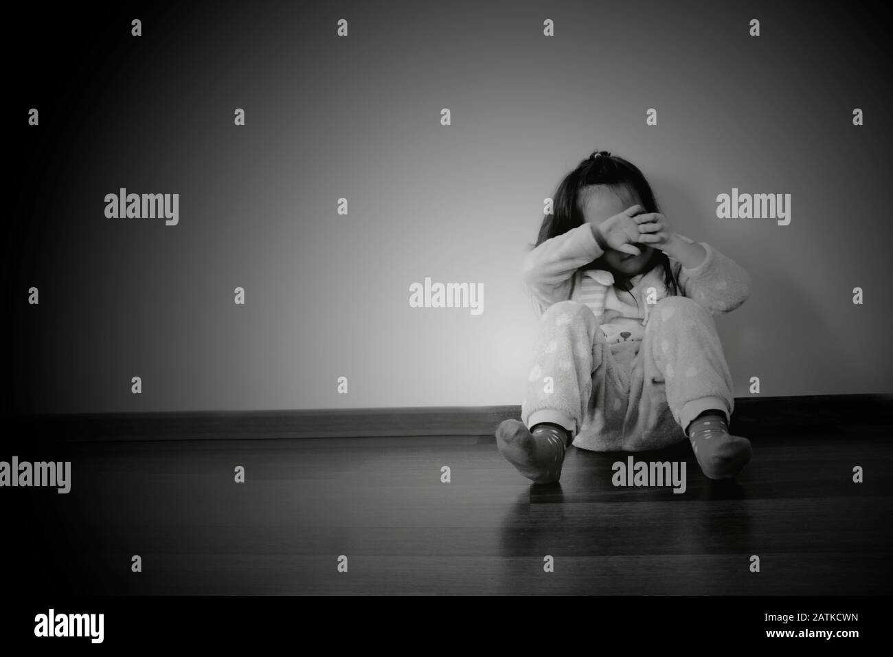 Trauriges kleines Mädchen, das auf dem Boden in schwarz-weißem Hintergrund sitzt Stockfoto