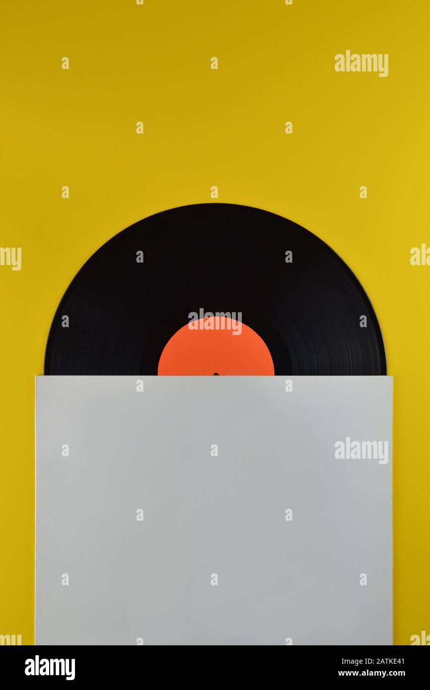 Alte schwarze Schallplatte mit leerem orangefarbenem Label, halb aus der weißen leeren Abdeckung auf gelbem Hintergrund Stockfoto