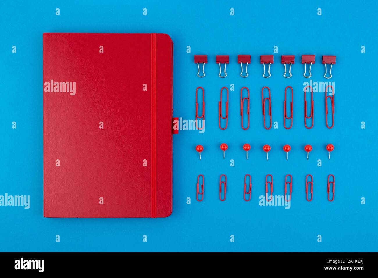 Red Business Notebook und Schreibwaren auf blauem Tisch. Zurück zur Schule oder zum Arbeitsplatz abstrakter Hintergrund. Minimale Zusammensetzung. Stockfoto