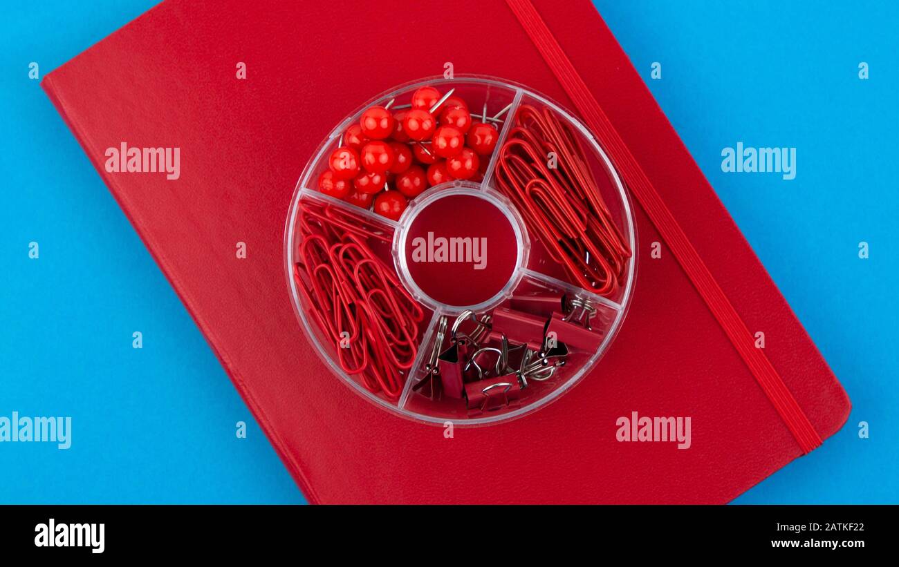 Red Business Notebook und Schreibwaren auf blauem Tisch. Zurück zur Schule oder zum Arbeitsplatz abstrakter Hintergrund. Minimale Zusammensetzung. Stockfoto